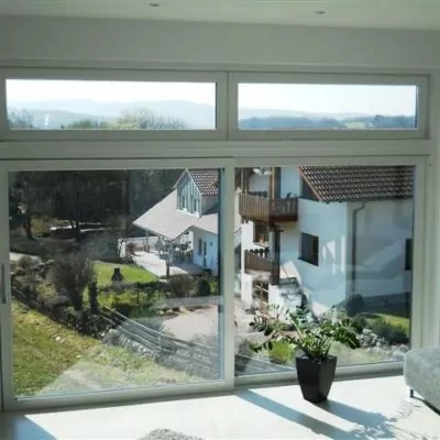 zwei-grosse-weisse-Fensterelemente-mit-Hebe-Schiebe-Tuer-mit-Ausblick-auf-Garten-und-Nachbarhaus